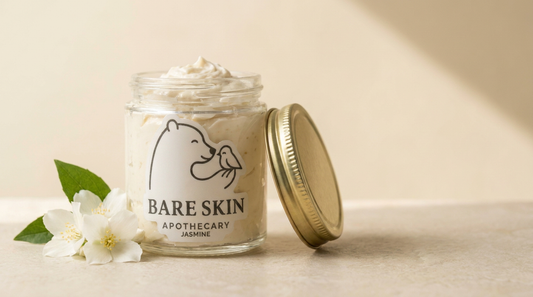 Jasmine Body Butter by Bare Skin Apothecary - whipped ivory body butter in a clear glass jar with gold lid and white die-cut label, jasmine blossoms